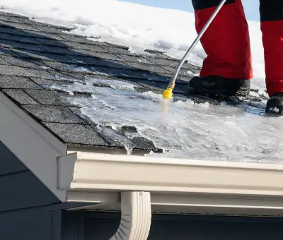 Ice dam removal technician using a steam wand to melt thick ice buildup on a residential roof in Albuquerque, NM
