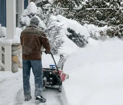 Residential snow removal technician using a snow blower to clear a home driveway and walkway in Albuquerque, NM