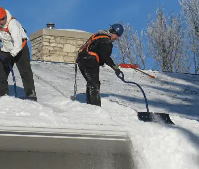 Professional technicians performing roof snow removal with safety harnesses and shovels in Albuquerque, NM